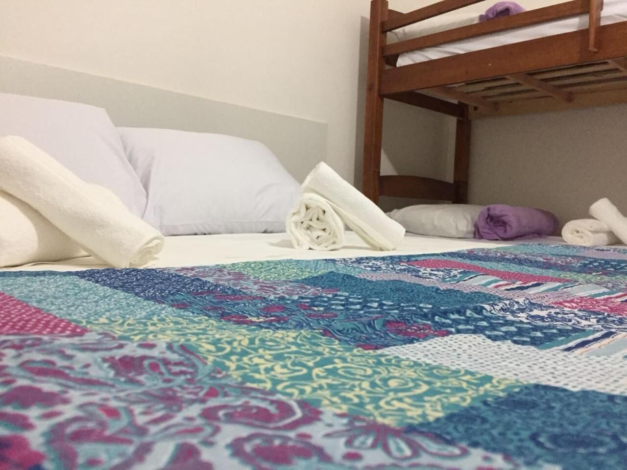 A bunk bed with a colorful quilt, a white pillow, and a rolled-up towel on the bed.