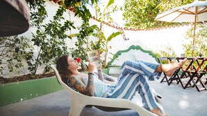 A person reclining on a white plastic chair outdoors, holding a book. - Pousada Arraial Caribe (Arraial do Cabo)
