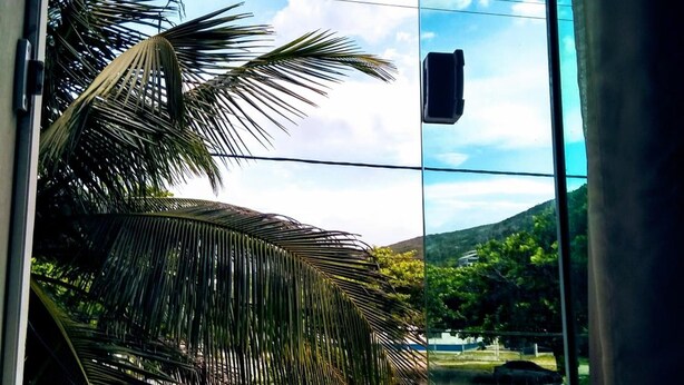 A window with a view of a palm tree and a clear sky. - Pousada Arraial Caribe (Arraial do Cabo)