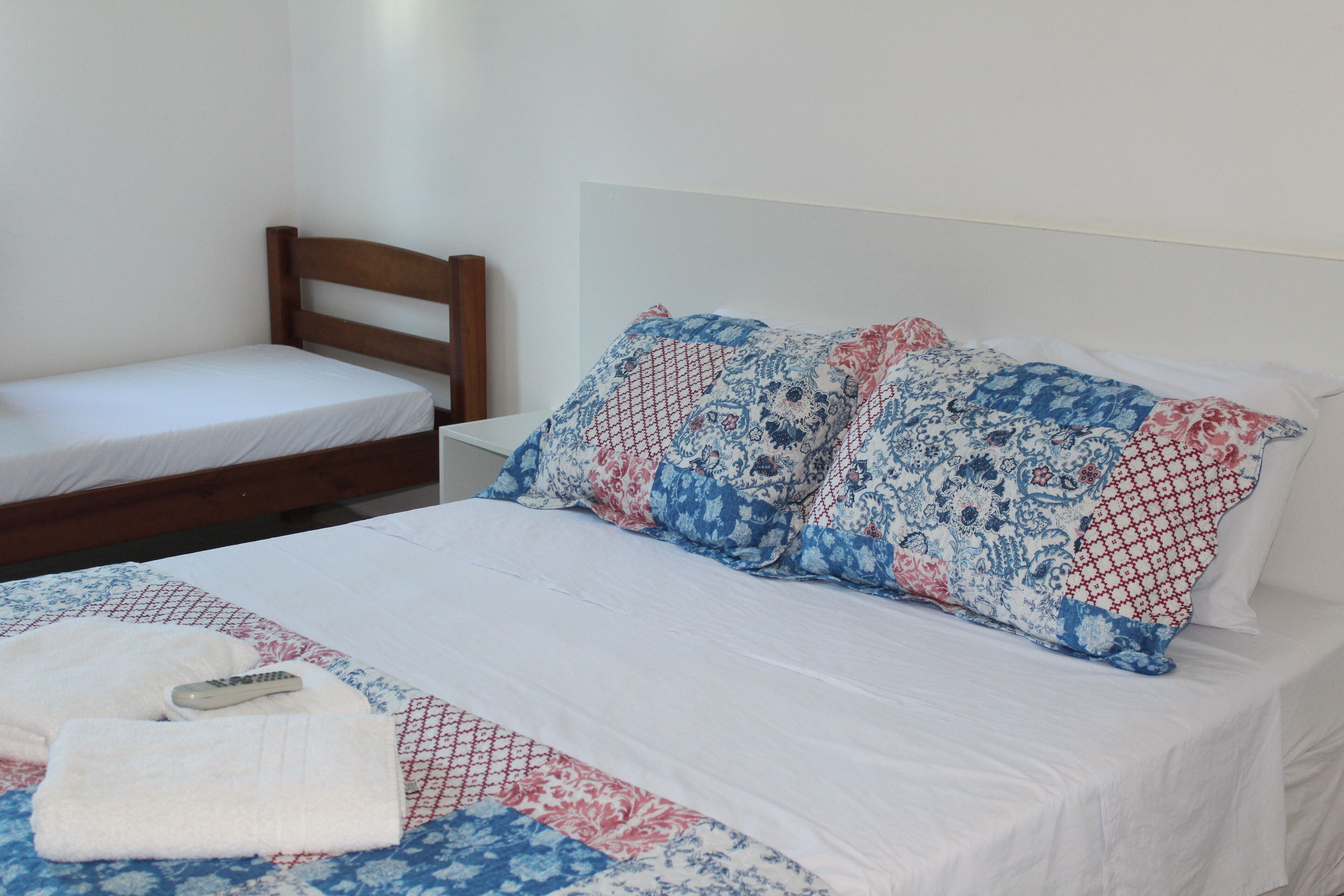 Una cama doble con sábana blanca y dos almohadas estampadas, cabecera de madera y mesita de noche blanca.