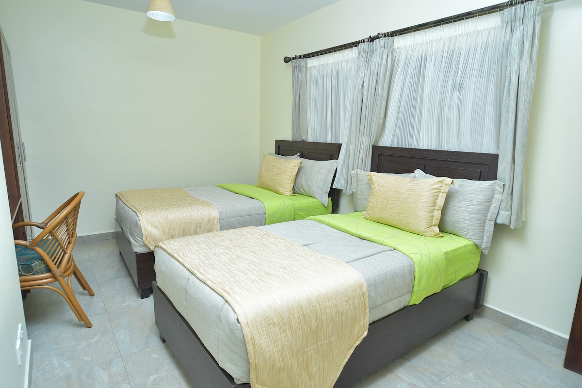 A bedroom with two beds, a wooden chair, and a ceiling light.