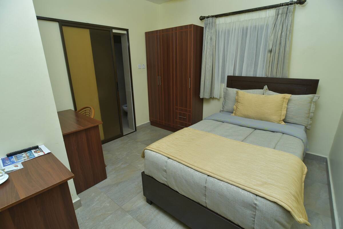 A bedroom with a bed, a wardrobe, a desk, and a door.