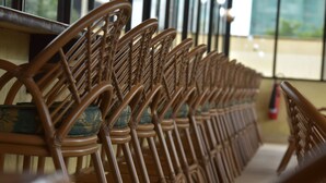 Eine Reihe aus Holzstühlen mit geflochtenen Rückenlehnen und gepolsterten Sitzflächen, ordentlich aufgereiht.
