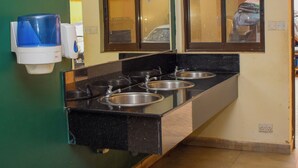 A public restroom with three sinks, a hand dryer, a trash bin, and a mirror. - Joy Palace (Nairobi)