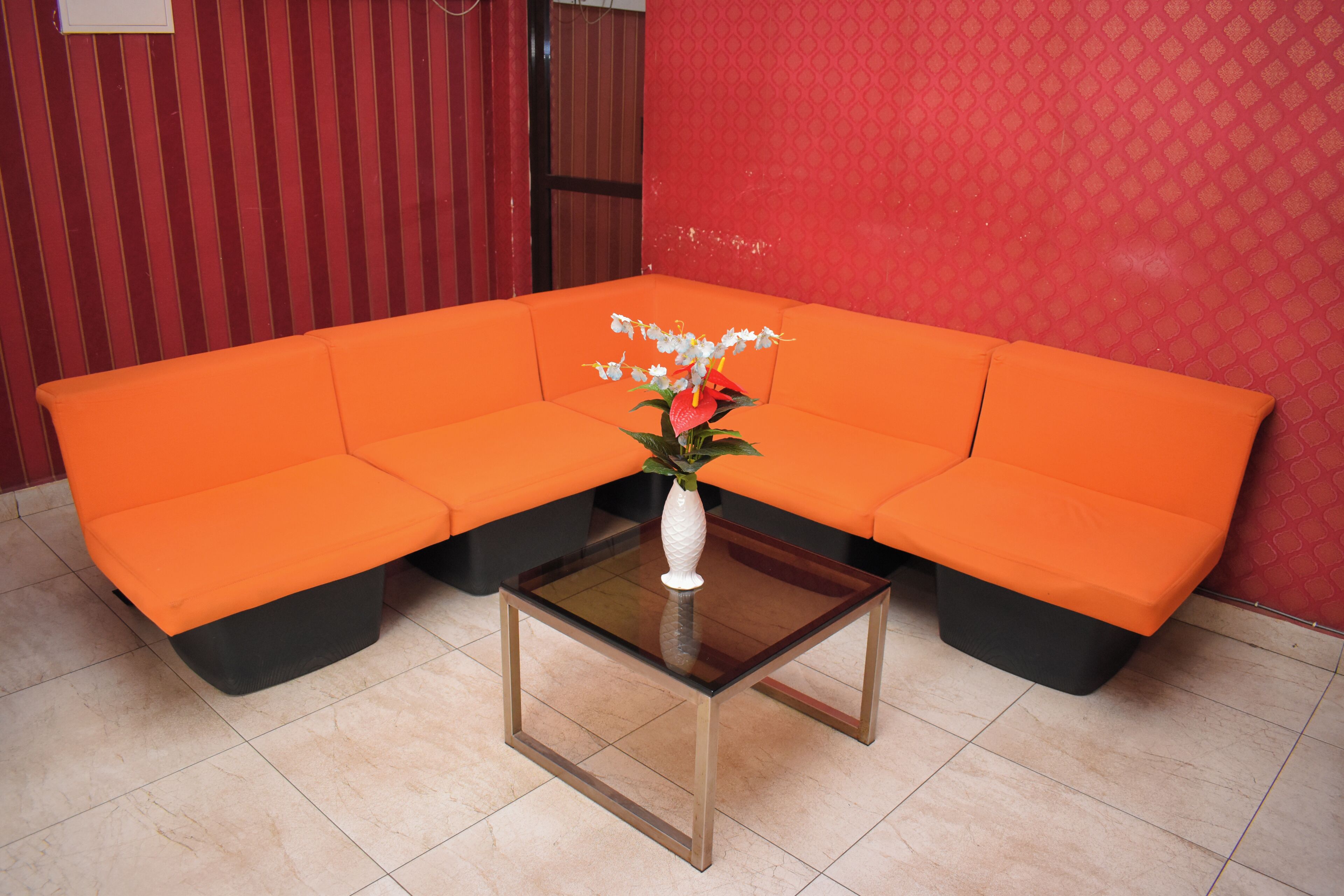 Un sofá modular en una esquina con una mesa de centro de vidrio y un jarrón blanco con flores.