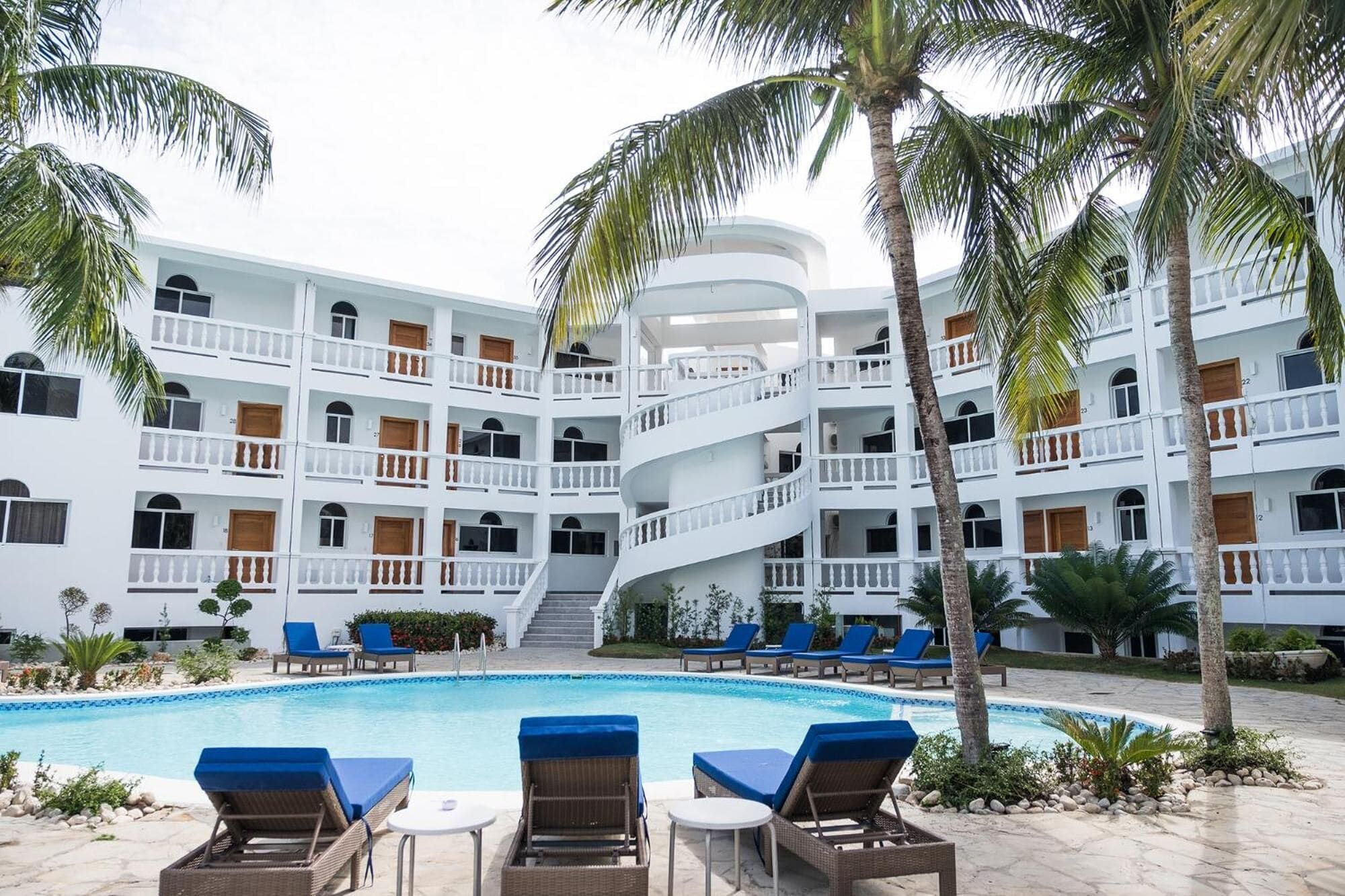 A multi-story hotel with a central pool surrounded by lounge chairs and palm trees.