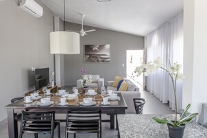 A modern dining area with a wooden table set for four, a ceiling fan, and a large window with curtains.