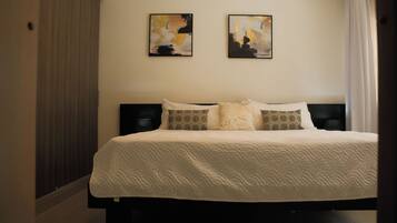 A neatly made bed with a white duvet, two pillows with a geometric pattern, and two abstract paintings on the wall.