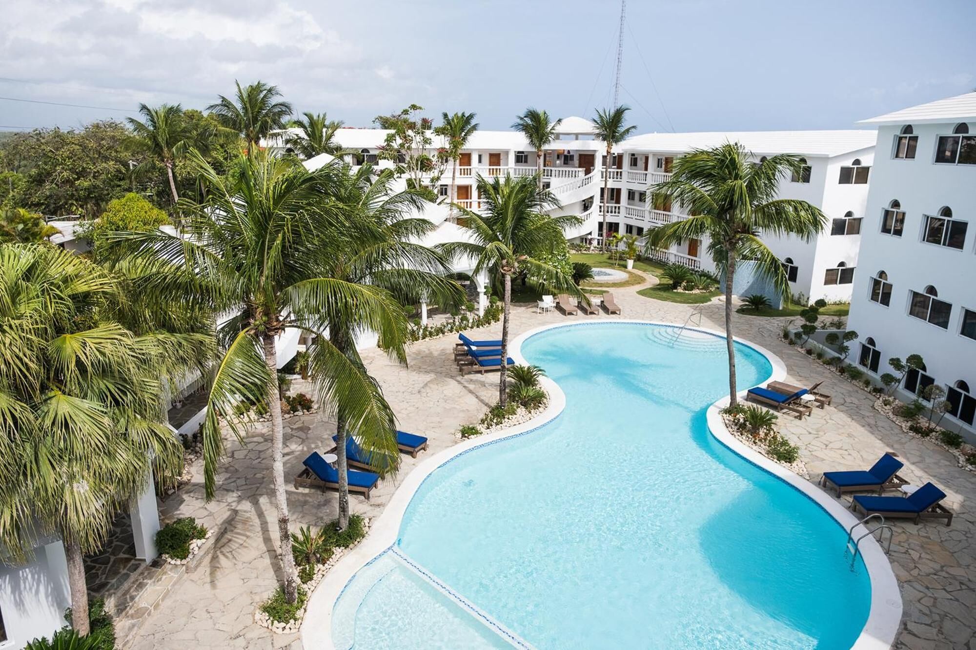 A resort with a curved pool surrounded by palm trees and lounge chairs.