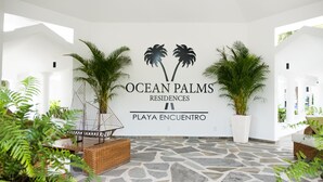 A spacious lobby with a stone floor, large potted plants, and a prominent sign for Ocean Palms Residences Playa Encuentro. - Ocean Palms Residences (Cabarete)