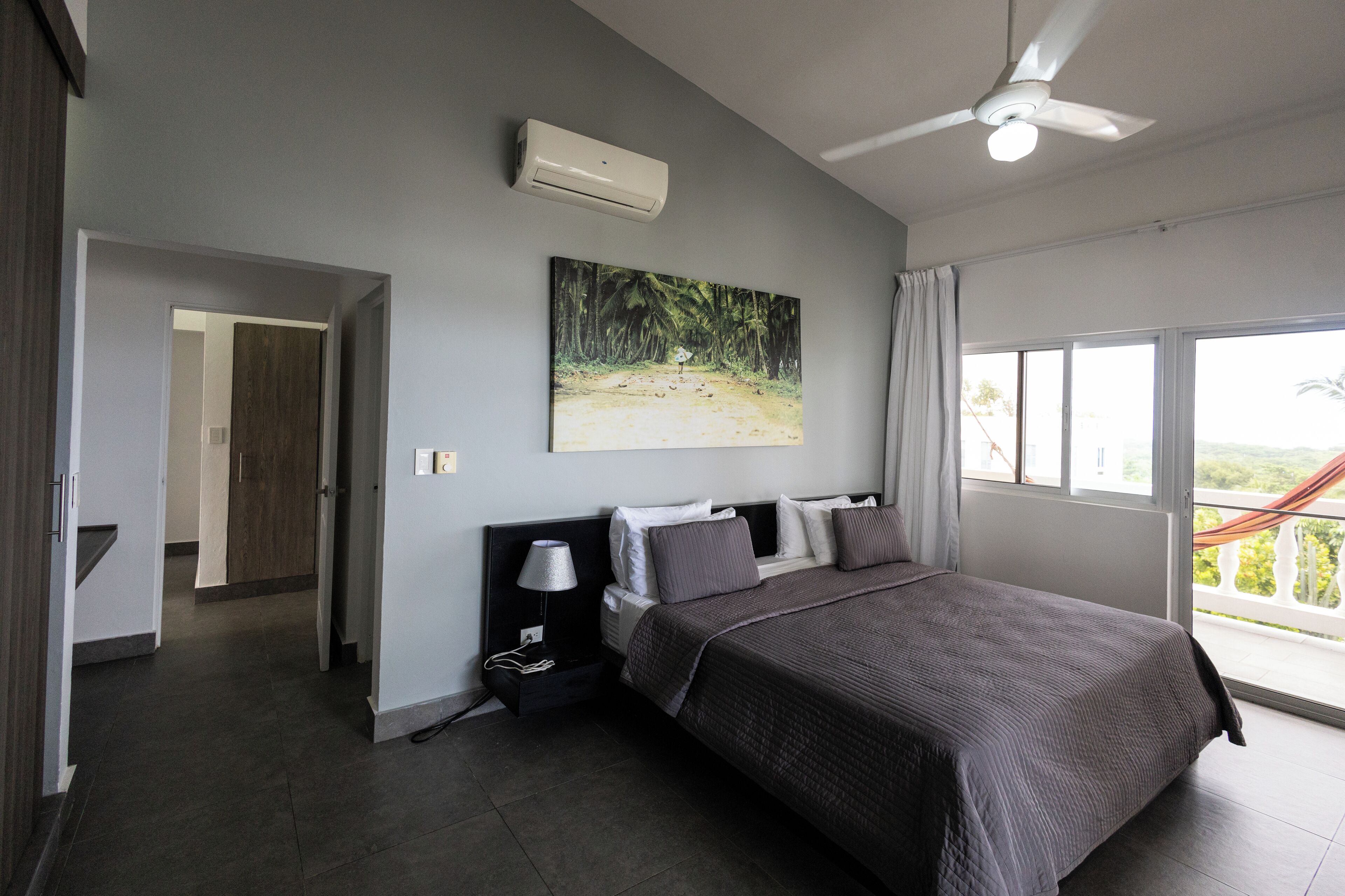 Une chambre moderne avec un grand lit, un ventilateur de plafond et une fenêtre donnant sur un paysage verdoyant.