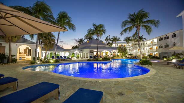 A swimming pool with lounge chairs and palm trees, surrounded by a building with multiple balconies. - Ocean Palms Residences (Cabarete)