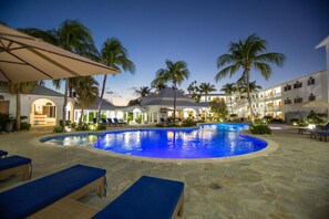 Piscina con sillas de descanso y palmeras, rodeada por un edificio con varios balcones.