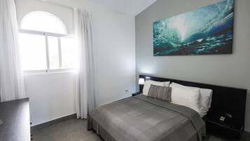 A modern bedroom with a large bed, a nightstand, a lamp, and a painting of a wave on the wall.