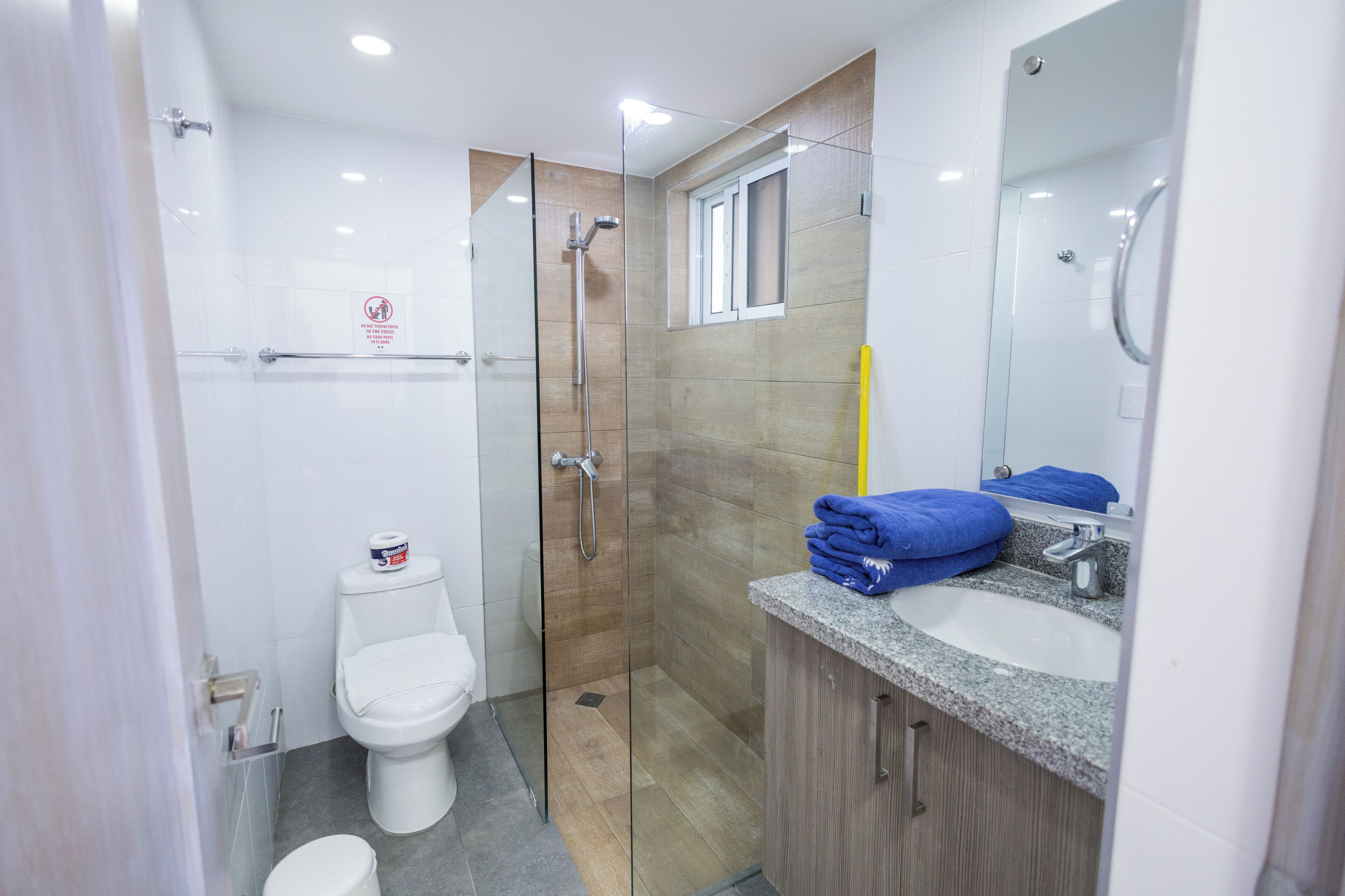 Un baño moderno con ducha envuelta en vidrio, inodoro blanco y encimera de granito con lavabo y espejo.