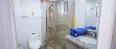 Un baño moderno con ducha envuelta en vidrio, inodoro blanco y encimera de granito con lavabo y espejo.