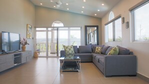 A modern living room with a grey sofa, a flat-screen TV, and a balcony with glass doors. - Ocean Palms Residences (Cabarete)