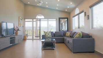 A modern living room with a grey sofa, a flat-screen TV, and a balcony with glass doors.