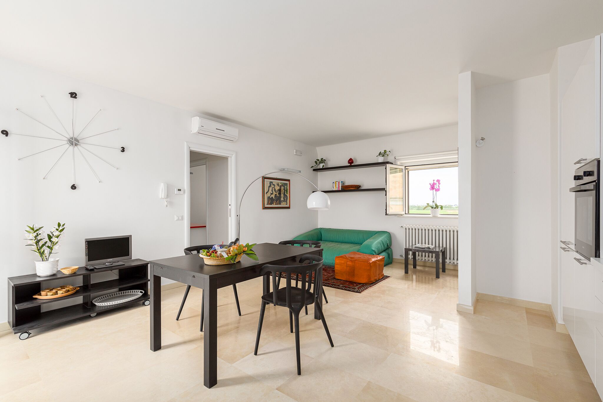 Una sala de estar moderna con comedor, un sofá verde, un televisor y un reloj decorativo en la pared.