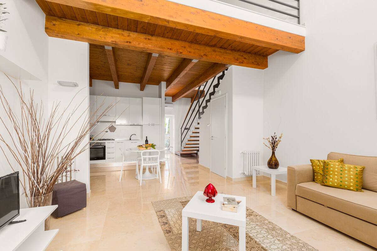 Ein modernes Wohnzimmer mit einer Couch, einem Couchtisch und einem Fernseher. Eine Treppe führt zu einer oberen Ebene.