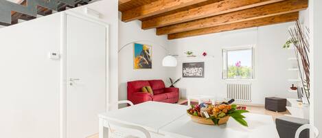 A modern living room with a white table, red sofa, and wooden ceiling beams.