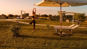 A person stretching outdoors with a white umbrella and lounge chairs in the background. - Tenuta Giardini Nuovi (Novoli)