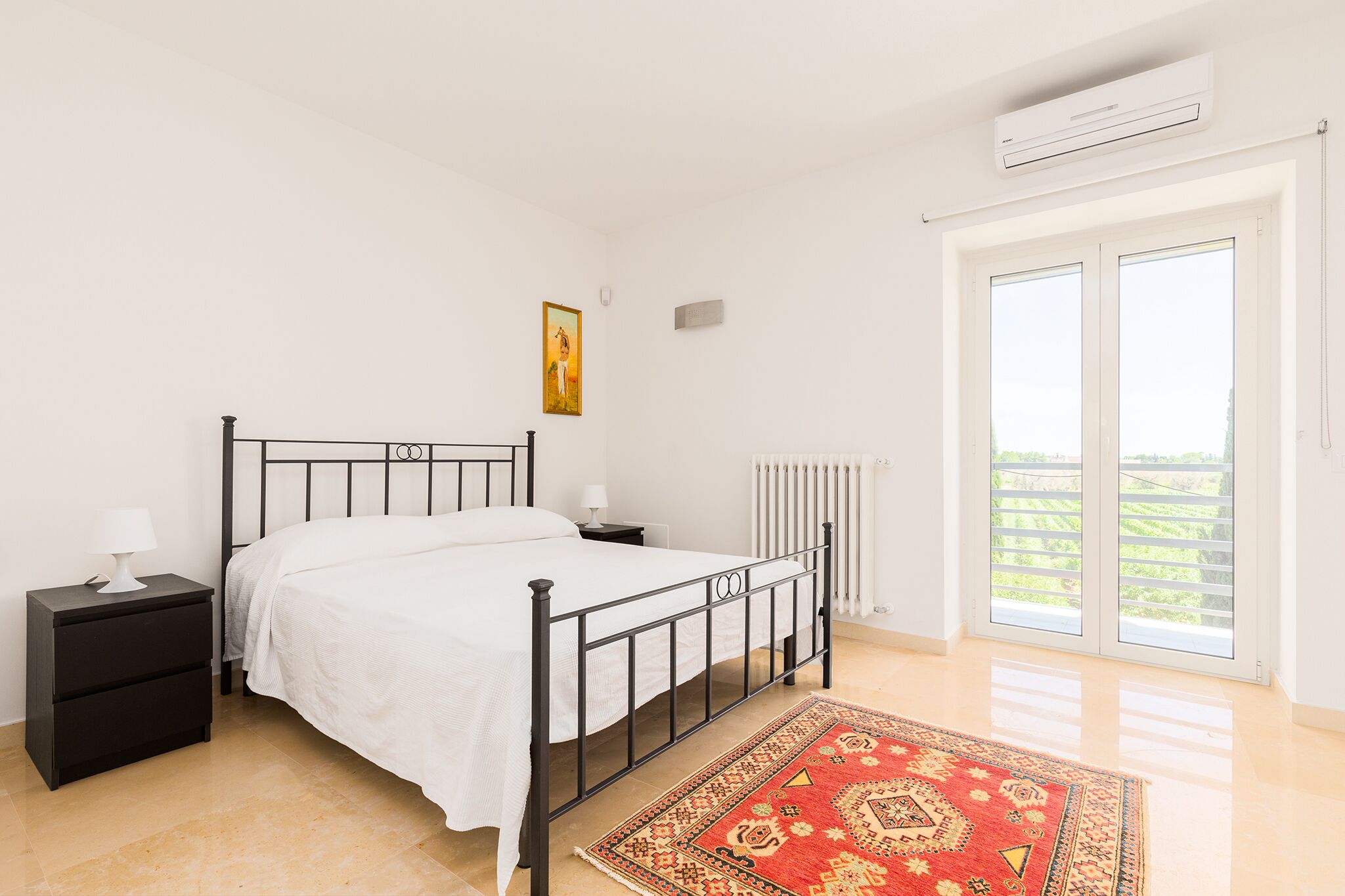 A bedroom with a bed, a nightstand, a radiator, a window with a view, and a ceiling fan.