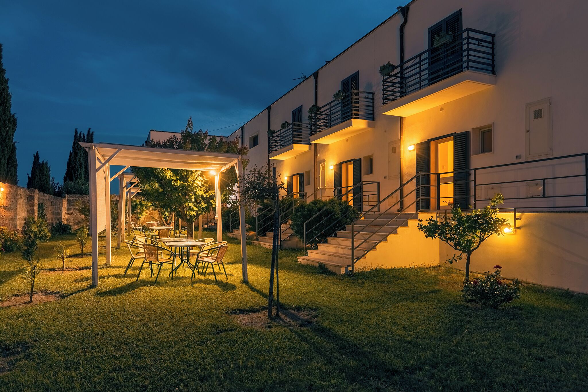 A modern building with a covered outdoor seating area, a staircase, and a well-maintained lawn.