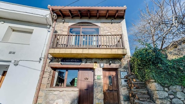 Un bâtiment en pierre de deux étages, doté d’un balcon en bois, d’une enseigne indiquant « CASA RURAL » et d’un mur en pierre surmonté d’une clôture en bois.