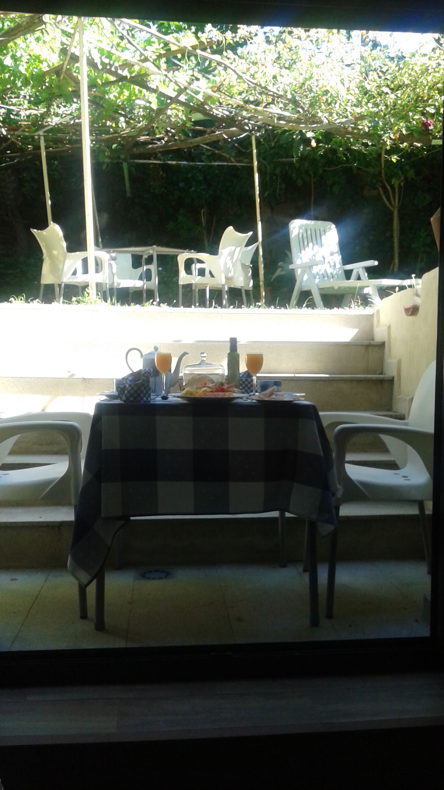 An outdoor dining area with a table set for two, surrounded by white plastic chairs.