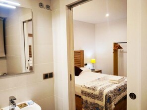 A hotel room with a bed, a bedside table with a lamp, a mirror, and a bathroom with a sink and toilet.