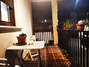 A small outdoor patio area with a table and chairs, potted plants, and a black metal fence.