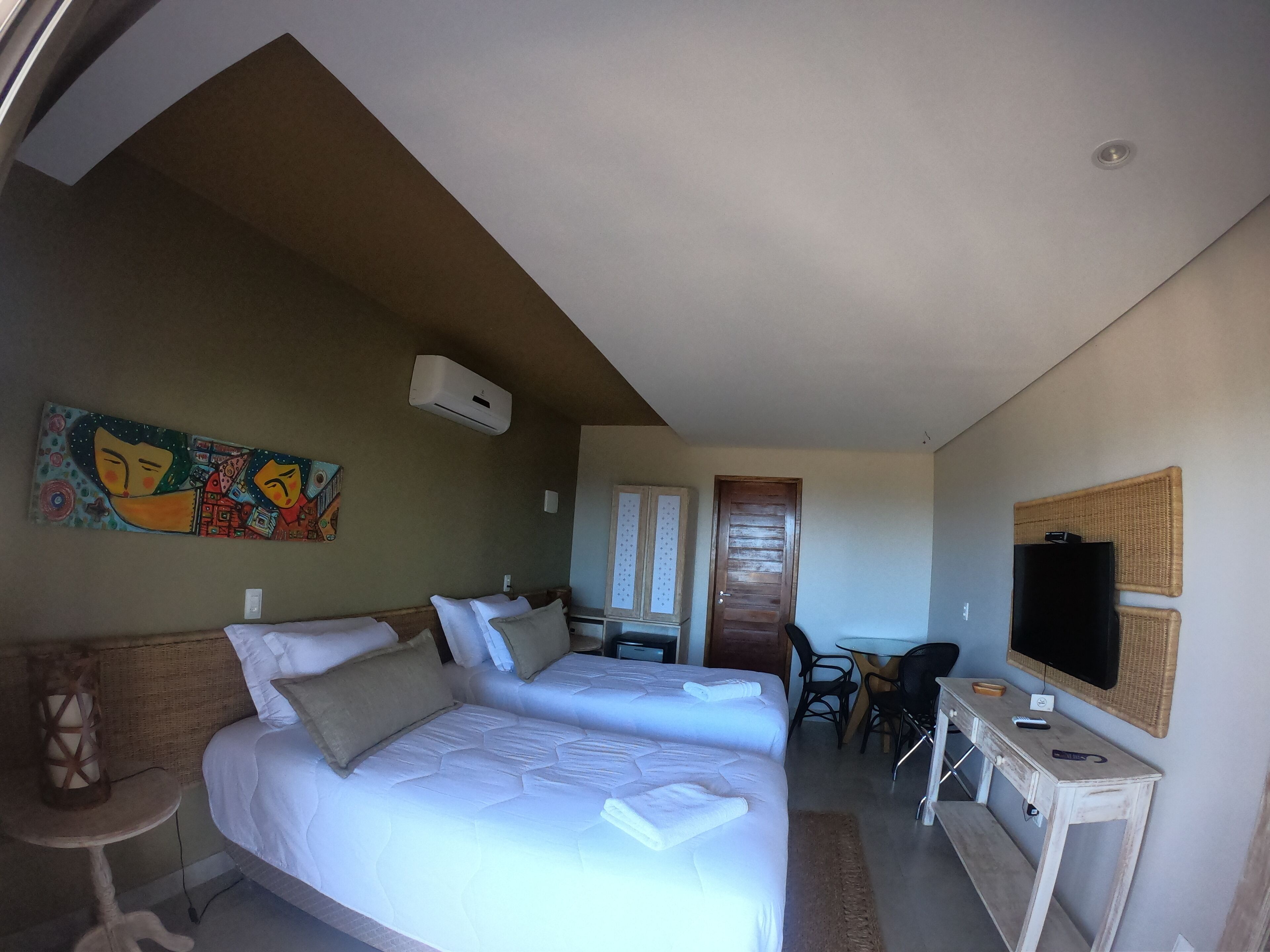 A hotel room with two beds, a desk, a TV, and a wall painting.