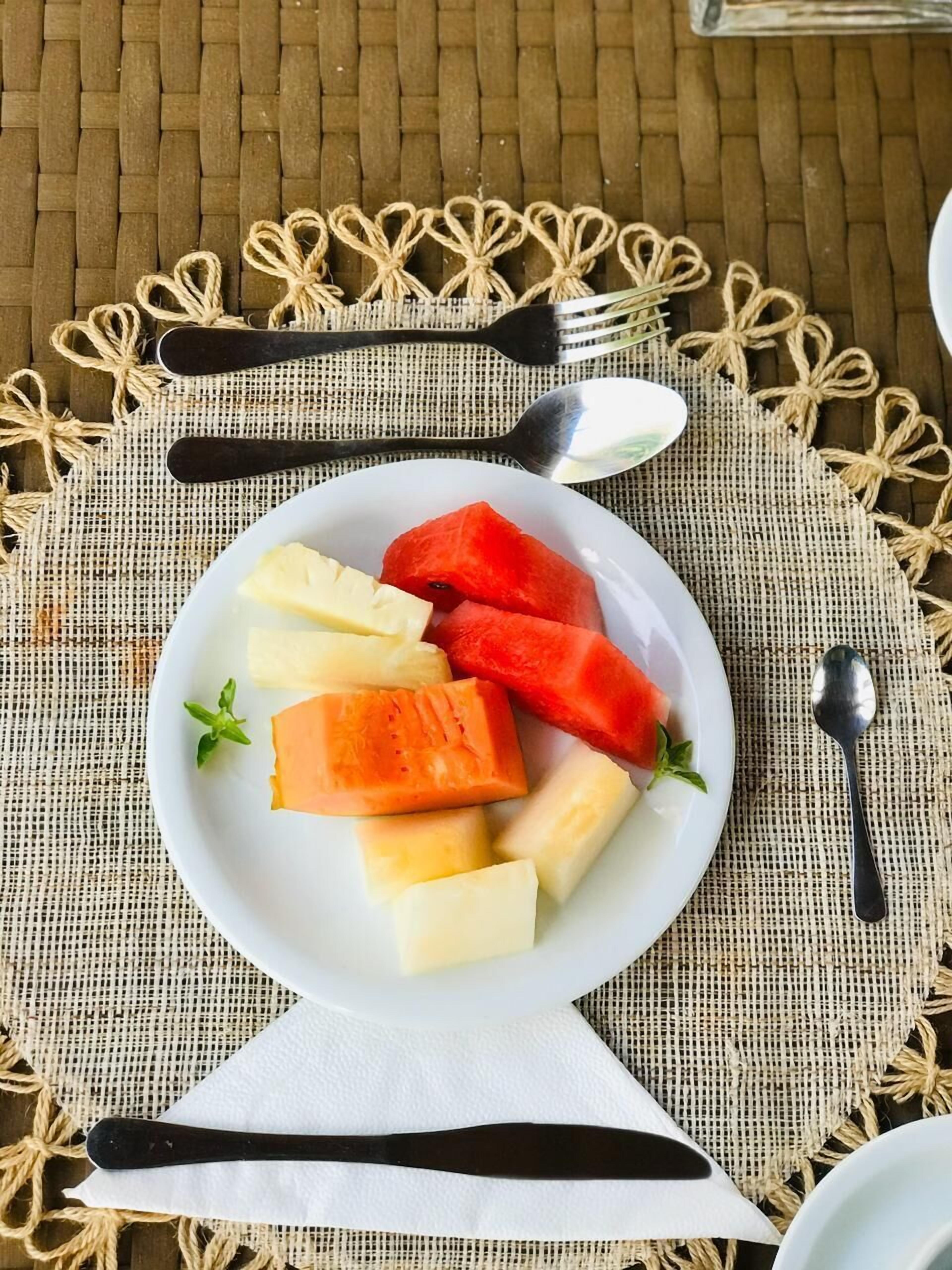 Une assiette blanche sur laquelle on a disposé des morceaux de pastèque, de melon et d’ananas, le tout posé sur un set de table en fibres tressées.