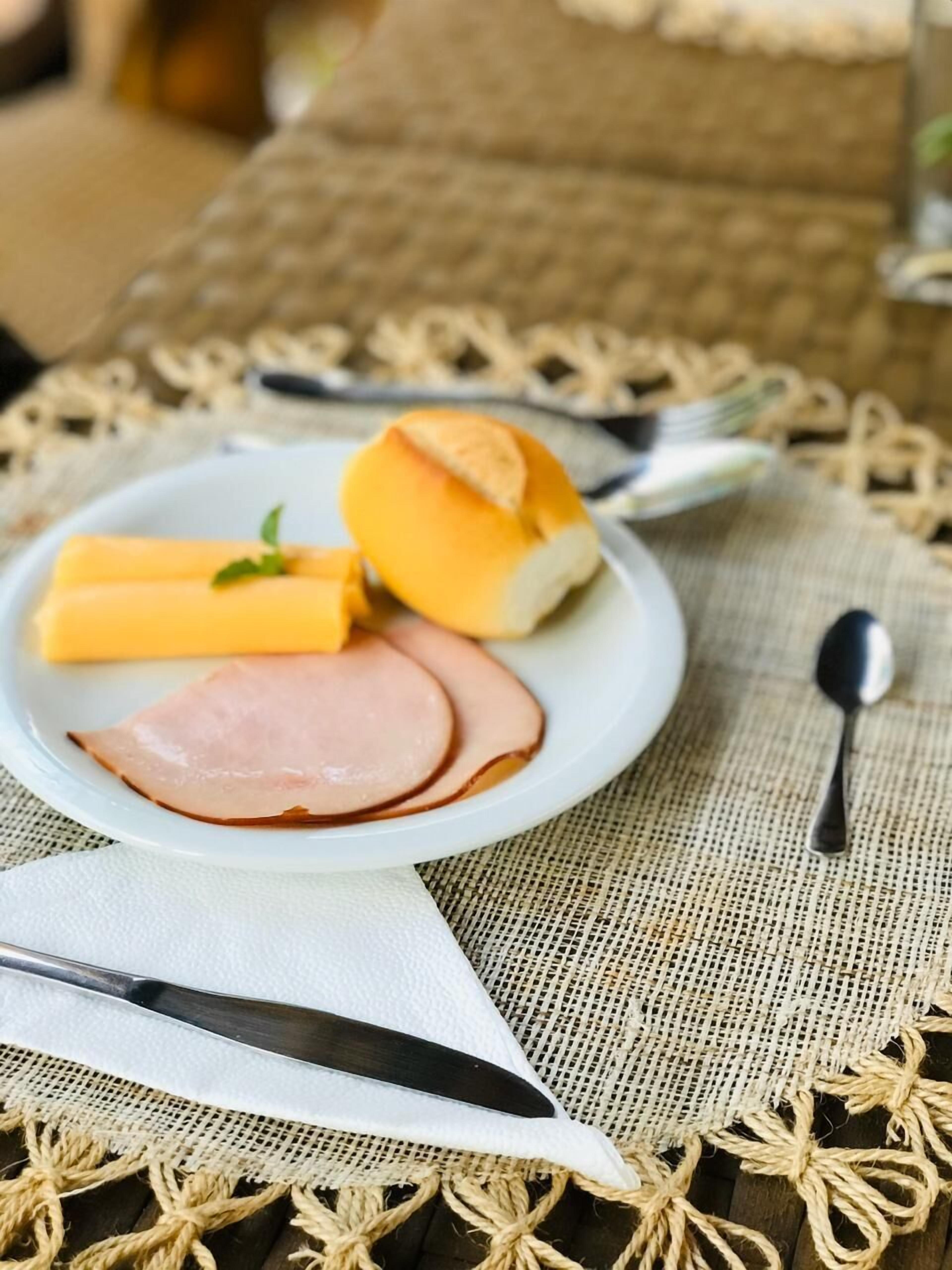 A plate with ham, cheese, and a roll on a table with a woven placemat.