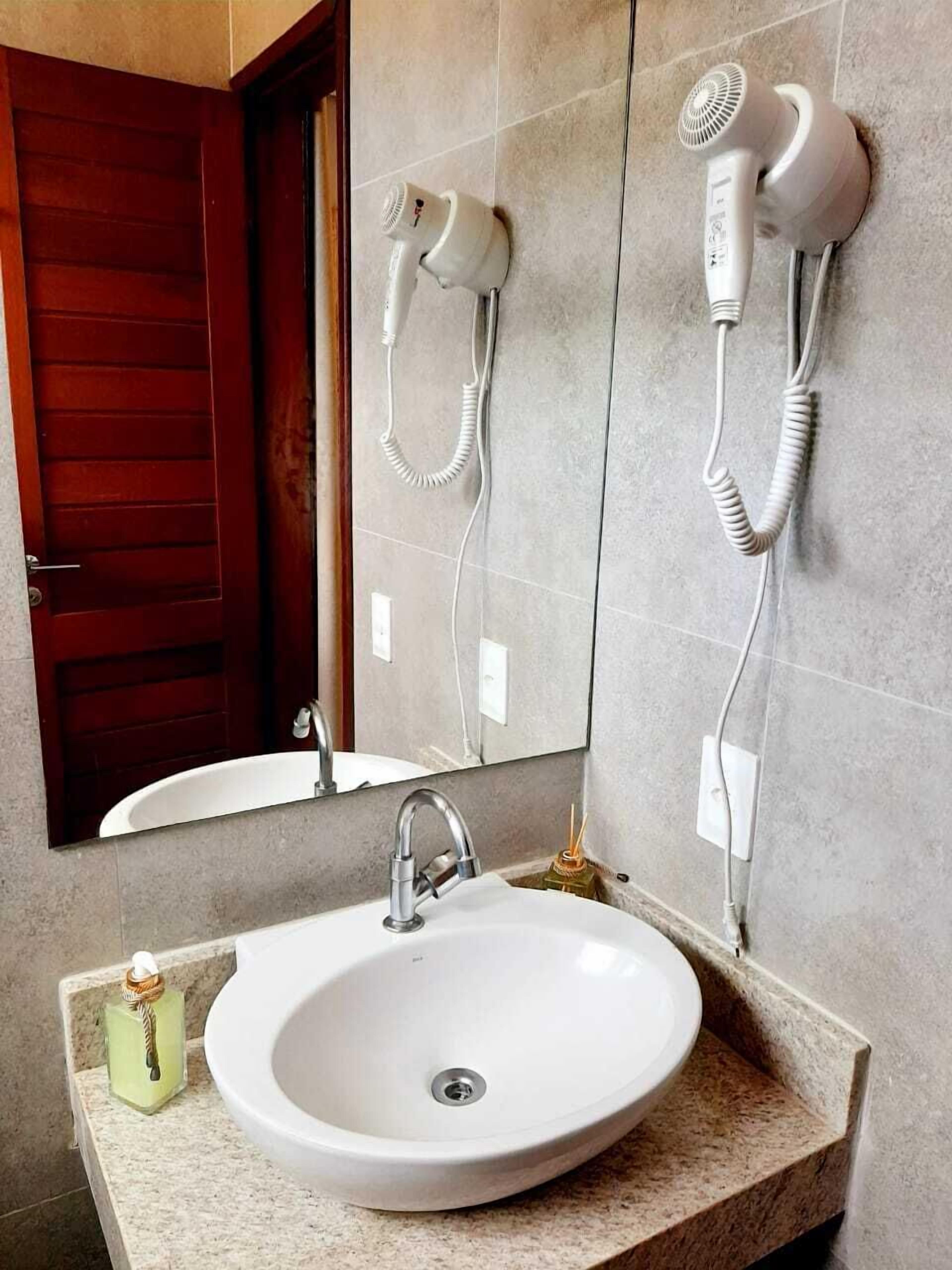 Une salle de bain avec un lavabo blanc, un miroir et deux sèche-cheveux fixés au mur.