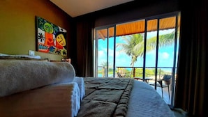 A hotel room with a large bed, a painting on the wall, and a view of palm trees through the window.