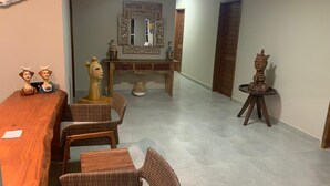 A dining area with a wooden table and wicker chairs, a decorative mirror, and a small round table with a statue.
