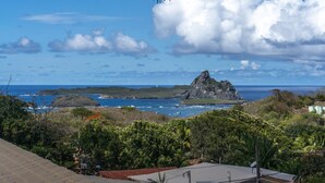 A coastal landscape with a prominent rock formation, lush greenery, and a view of the ocean.