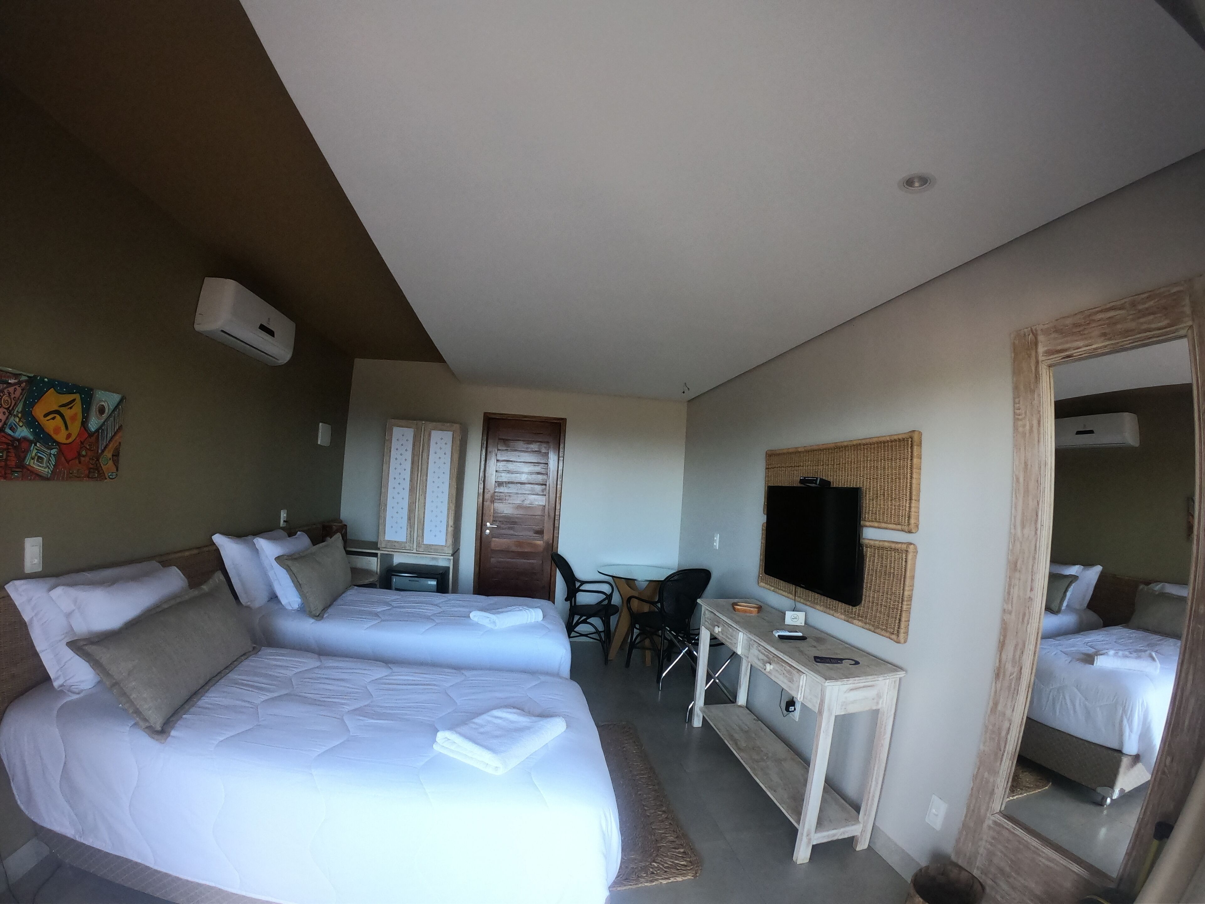 A hotel room with two beds, a desk, a chair, a TV, and a mirror.