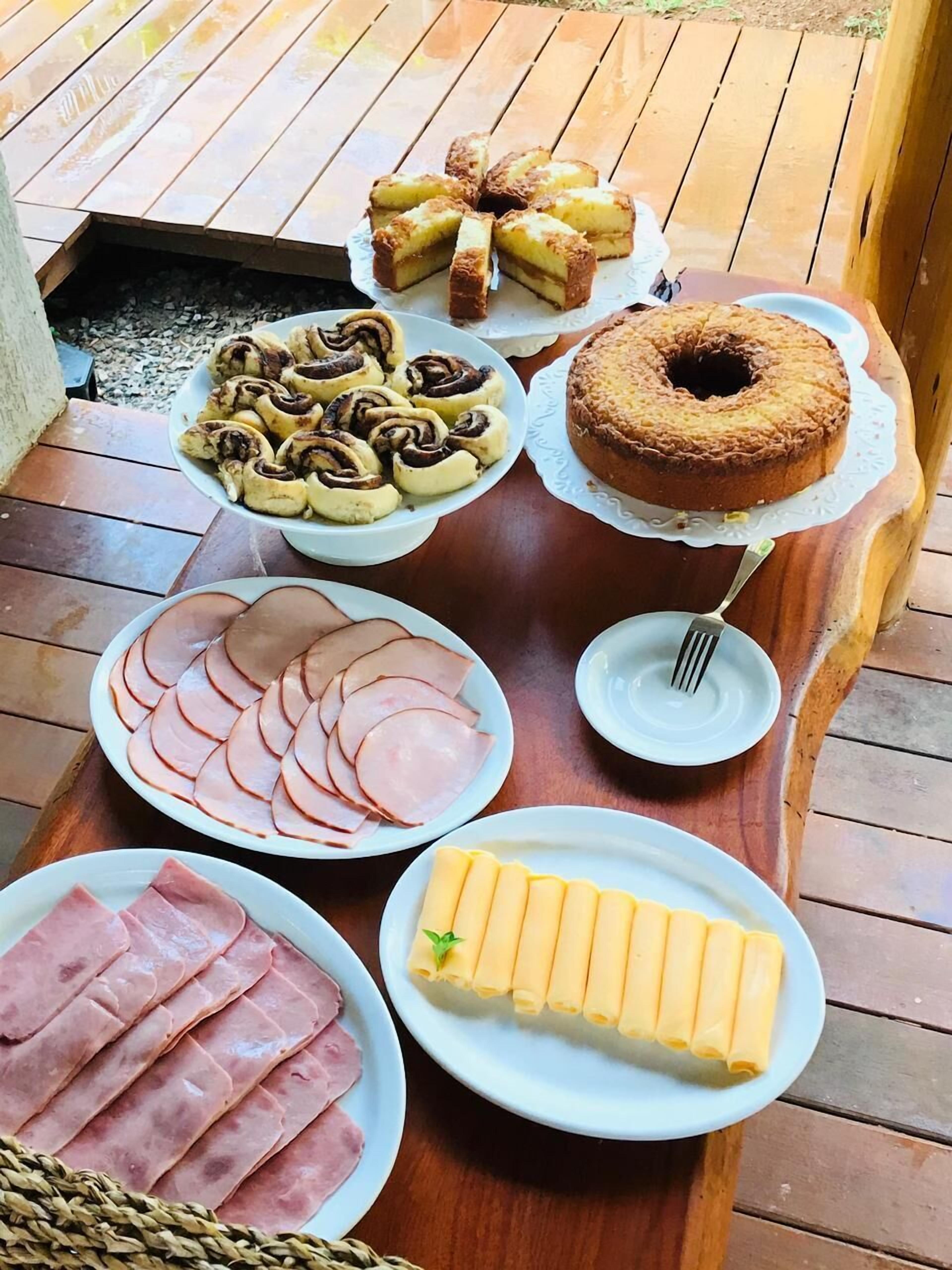 A wooden table with various food items including sliced ham, cheese, pastries, and a bundt cake.