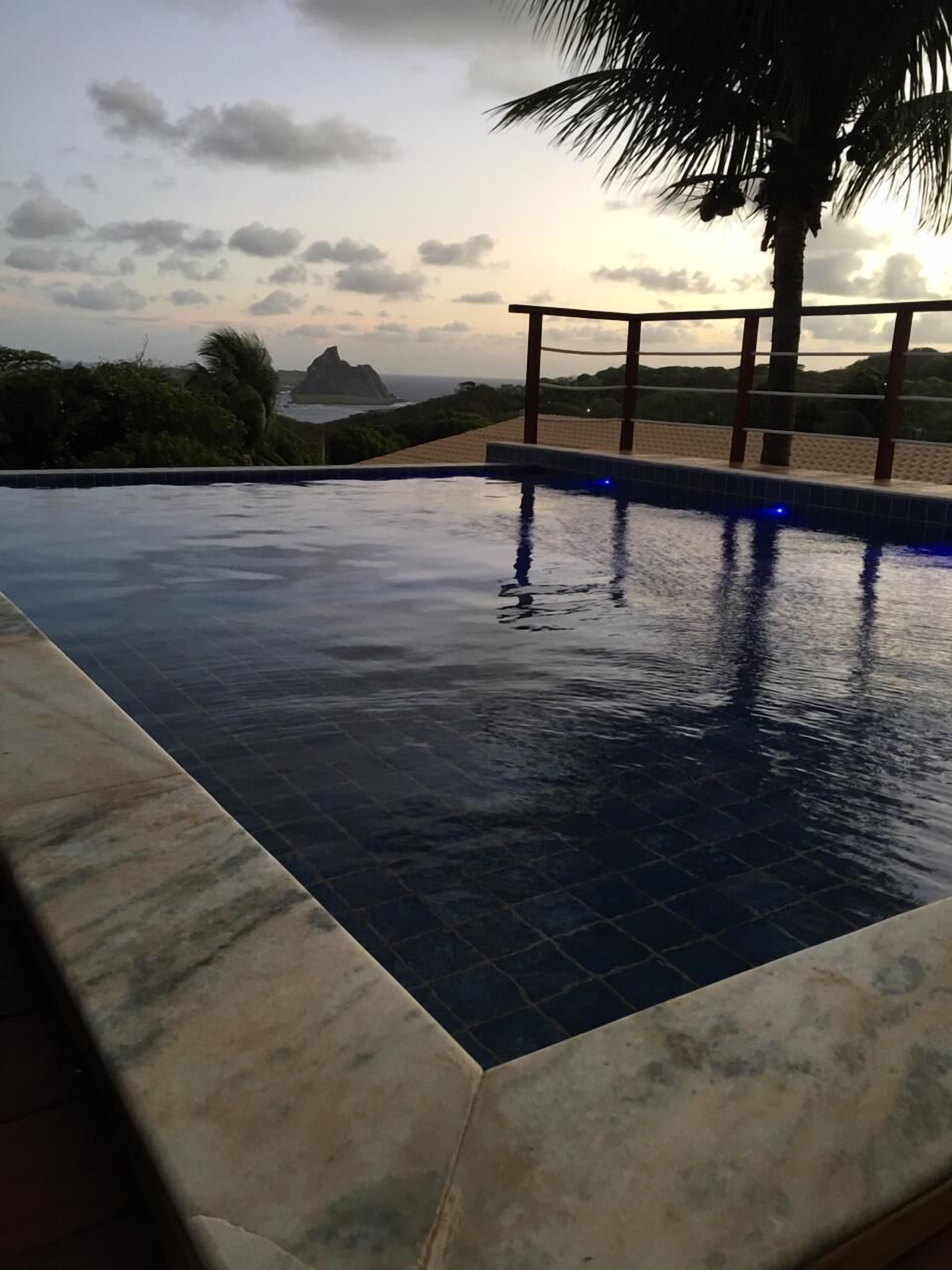A swimming pool with a view of the ocean and hills at sunset.