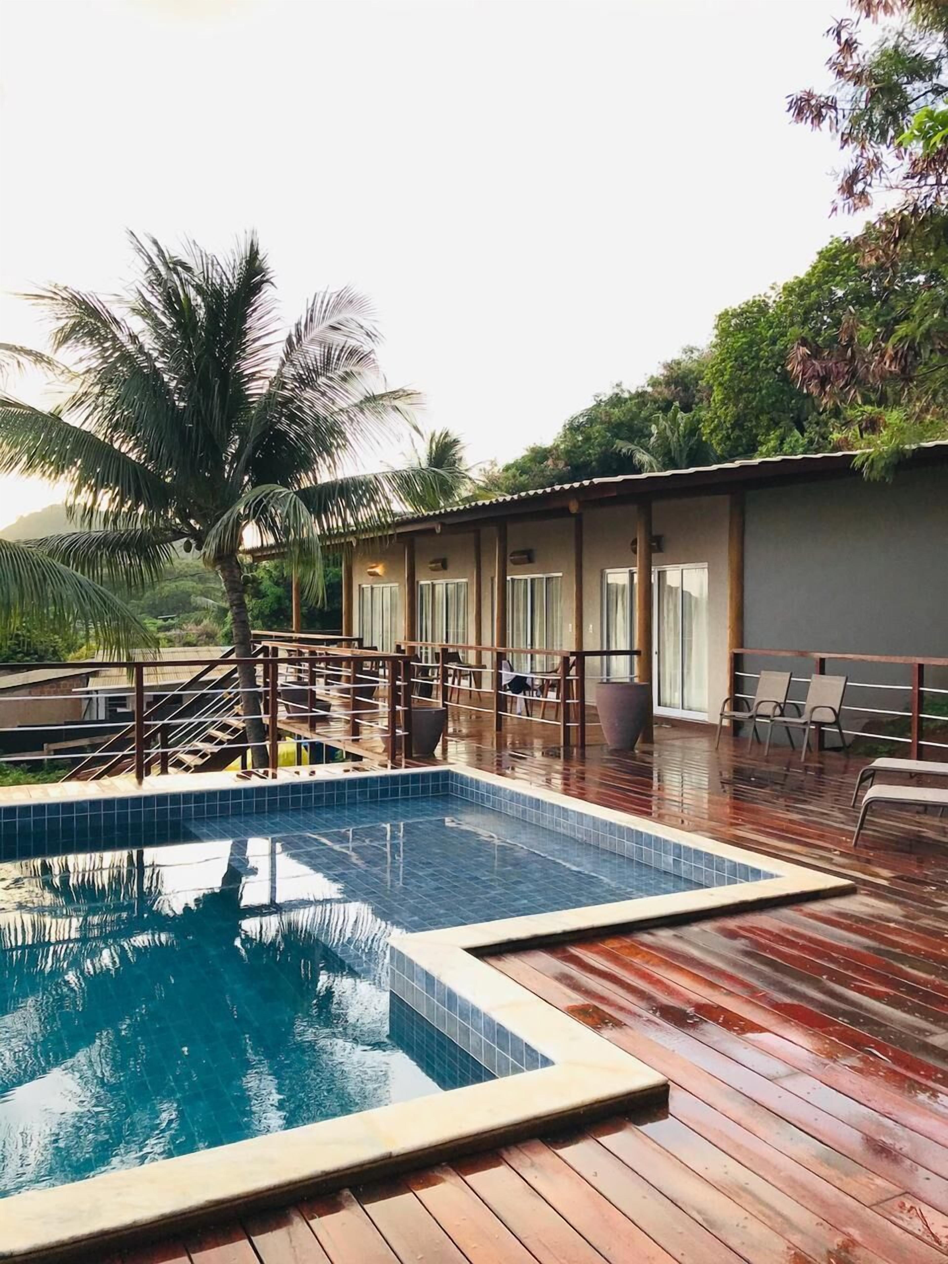 A swimming pool with a wooden deck, palm trees, and a building with large windows.