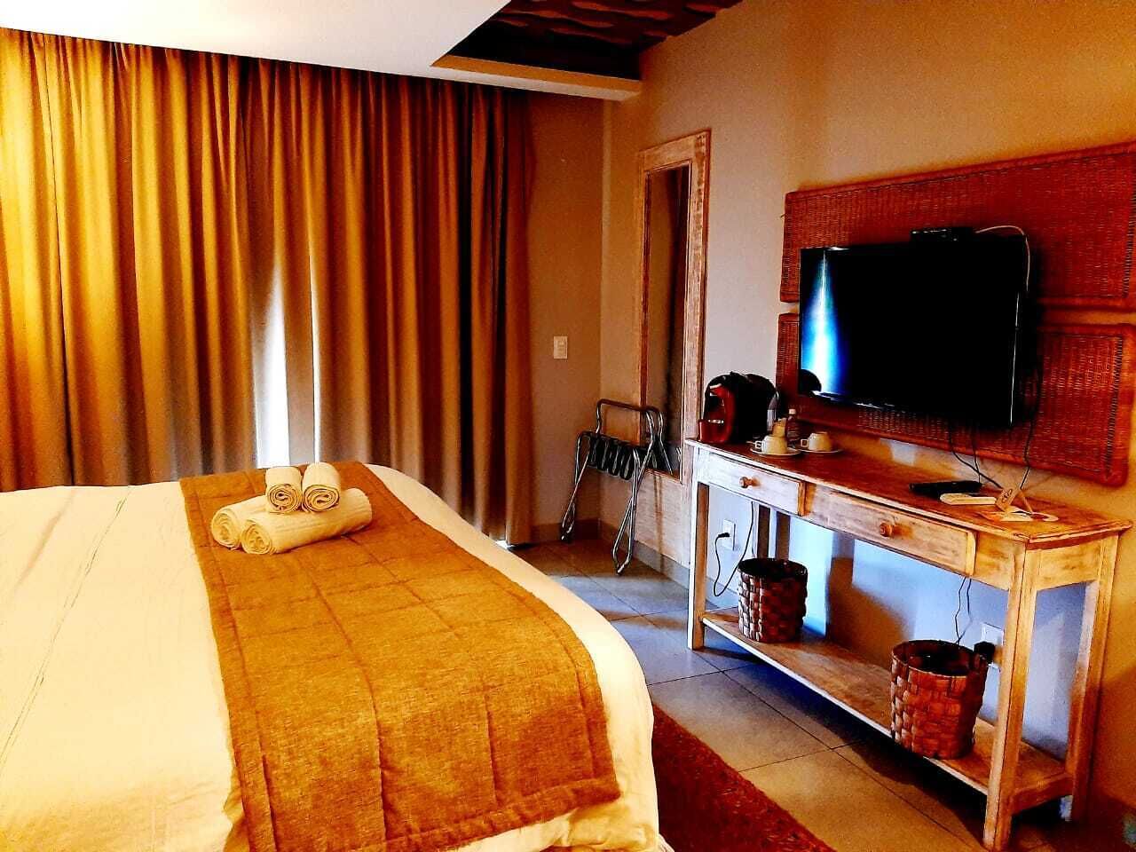 A hotel room with a bed, a television on a wooden stand, and a window with curtains.