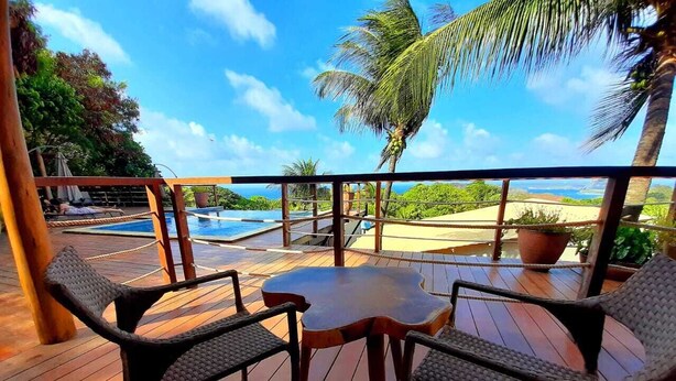 A wooden deck with a round table and two chairs, overlooking a pool and palm trees.