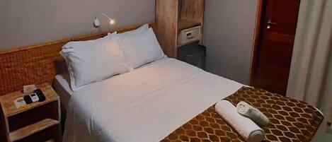 A neatly made bed with a patterned bedspread, a bedside table with a lamp, and an air conditioning unit on the wall.