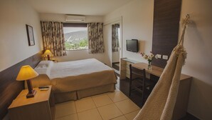 Una habitación de hotel con cama, escritorio, televisión y ventana con cortinas.
