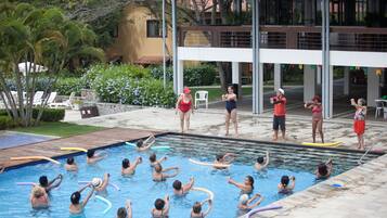 Uma área de piscina com várias pessoas praticando atividades aquáticas, cercada por um edifício com varanda e área de estar externa.