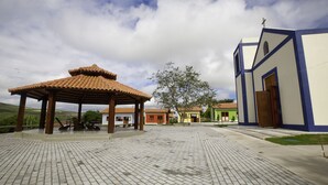 Un patio empedrado con un pabellón, un edificio con cruz en la parte superior y algunas casas pequeñas al fondo.
