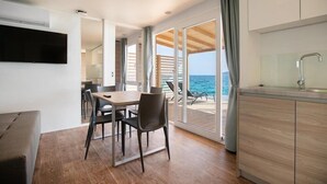 Una cocina moderna con horno empotrado, un comedor con mesa y sillas, y vista al mar a través de puertas de cristal grandes.